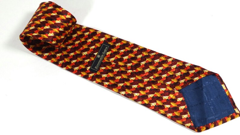 May include: A red, orange, and gold patterned silk tie with a navy blue lining. The tie has a label that reads "Ermenegildo Zegna".