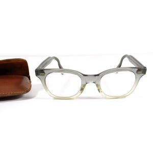 May include: A pair of gray plastic eyeglasses with a brown leather case.