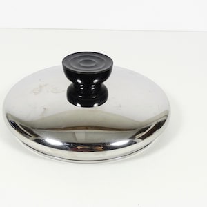 May include: A silver pot lid with a black knob. The lid is round and has a shiny surface.