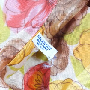 Pode incluir: Close-up de um tecido branco com estampa floral em tons de laranja, amarelo e verde. O tecido tem uma etiqueta que diz "100% Acetato Feito no Jap&atilde;o HPL 6119".