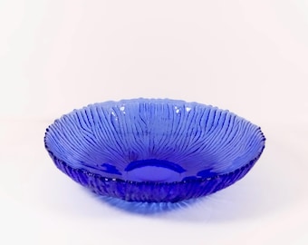May include: A vibrant blue glass bowl with a textured, ridged pattern. The bowl has a wide, shallow design and a slightly scalloped rim. The color is a deep, saturated blue, and the bowl is set against a white background.