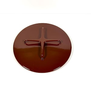 May include: A circular, deep brown lid with a glossy finish. The top surface features a centered, raised cross-shaped handle with rounded edges, designed for easy gripping. The lid has a smooth, uniform appearance with no visible markings or text.