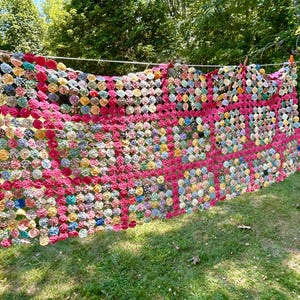 May include: A large quilt constructed from numerous small, circular fabric patches stitched together. The quilt features a repeating grid pattern of vibrant magenta fabric circles interspersed among a variety of multi-colored floral and patterned circles.