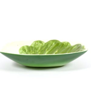 May include: A green and white ceramic bowl with a wavy design. The bowl is shaped like a leaf and has a glossy finish.