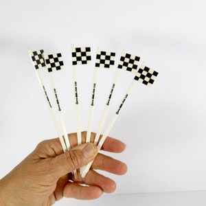 May include: Six black and white checkered flags on white sticks. The sticks are labeled "Gama Silk - Next Day"