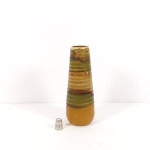May include: A tall, brown, green, and yellow ceramic vase with a striped pattern. The vase is on a white surface.