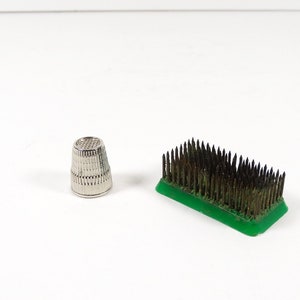 May include: A silver thimble and a green floral foam block with metal pins.