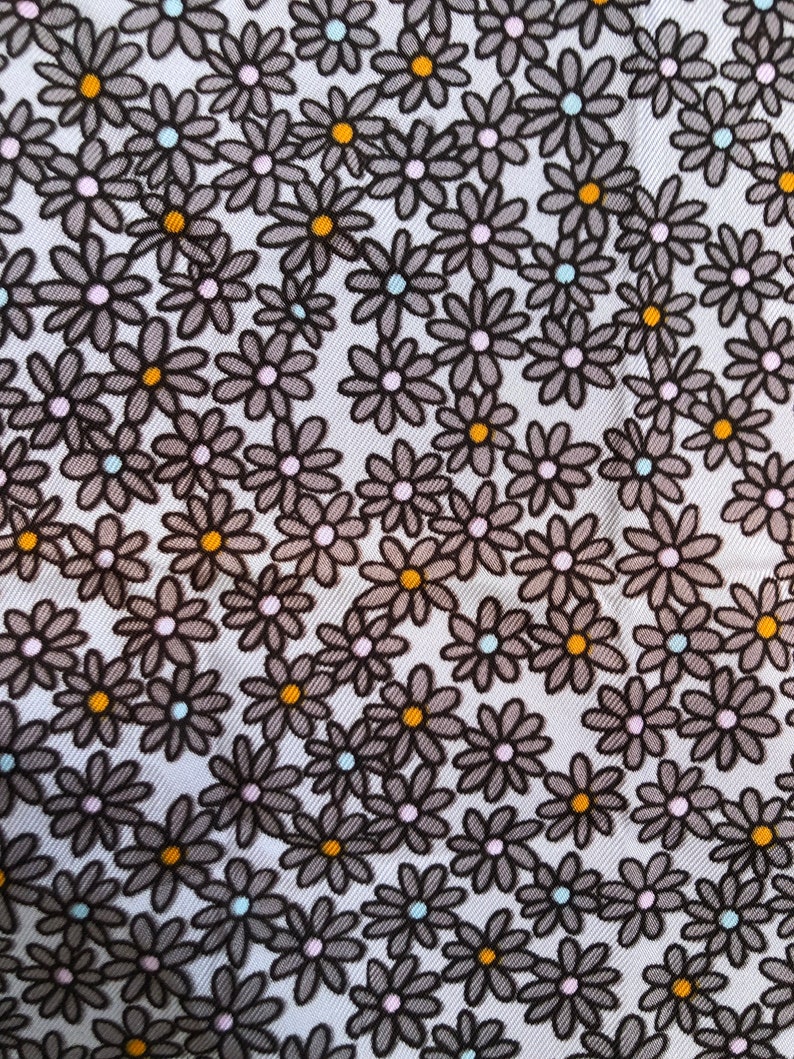 Puede incluir: Primer plano de una tela con un estampado floral repetido. Las flores son grises con contornos negros y tienen centros amarillos, rosas y celeste. El fondo es blanco.