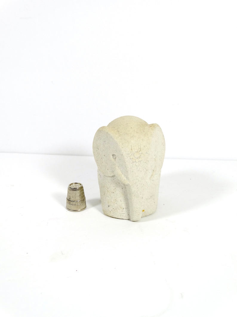 Peut inclure: Une petite figurine d'&eacute;l&eacute;phant en pierre blanche. L'&eacute;l&eacute;phant est debout sur une surface blanche.