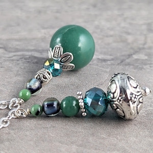 May include: A green stone bead necklace with silver and blue glass beads. The necklace has a large green stone bead at one end and a silver bead with a decorative design at the other end.