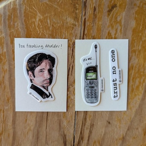 May include: Set of three stickers featuring imagery from the X-Files. One sticker depicts Fox Mulder with the text "Fox freaking Mulder!". Another shows a Nokia phone with "It's me... Scully" and the third says "trust no one".