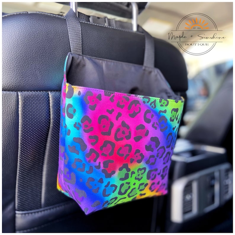 May include: A rainbow tie-dye fabric car seat organiser with a black leopard print. The organiser is hanging from the headrest of a car seat.