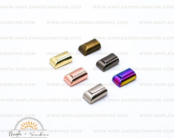 May include: Five metal bag or purse hardware pieces in different finishes: gold, brass, rose gold, silver, and iridescent. The hardware pieces are all the same shape, with a rounded top and a flat bottom.