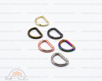 May include: Six different colored metal D-rings. The rings are in various colors, including gold, bronze, black, rose gold, rainbow, and silver.
