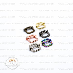 May include: A collection of square metal slider buckles in various colors, including gold, bronze, silver, rose gold, black, and rainbow. The buckles are arranged on a white background. The Maple + Sunshine Boutique logo is in the bottom left.