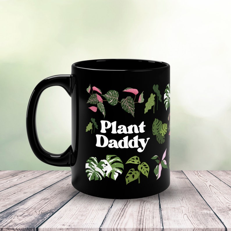 May include: Black ceramic mug with a white graphic that says "Plant Daddy" surrounded by green and pink plant illustrations.