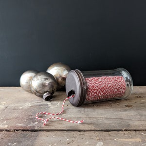 red and white double twisted baker's string or twine roll housed in a glass sugar dispenser with a hand painted bronze toned lid