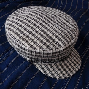 May include: A black and white checkered fabric cap with a slightly curved brim. The cap is on a blue and white striped fabric background. The text "THE GREEN TREE" is visible at the bottom of the image.