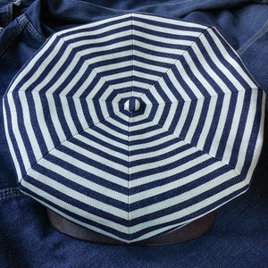 May include: A white and navy blue striped octagonal hat with a button on top.