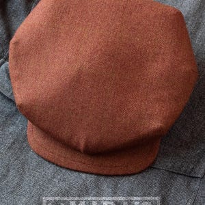 Puede incluir: Una gorra de newsboy de tweed marr&oacute;n con un patr&oacute;n de espiga.