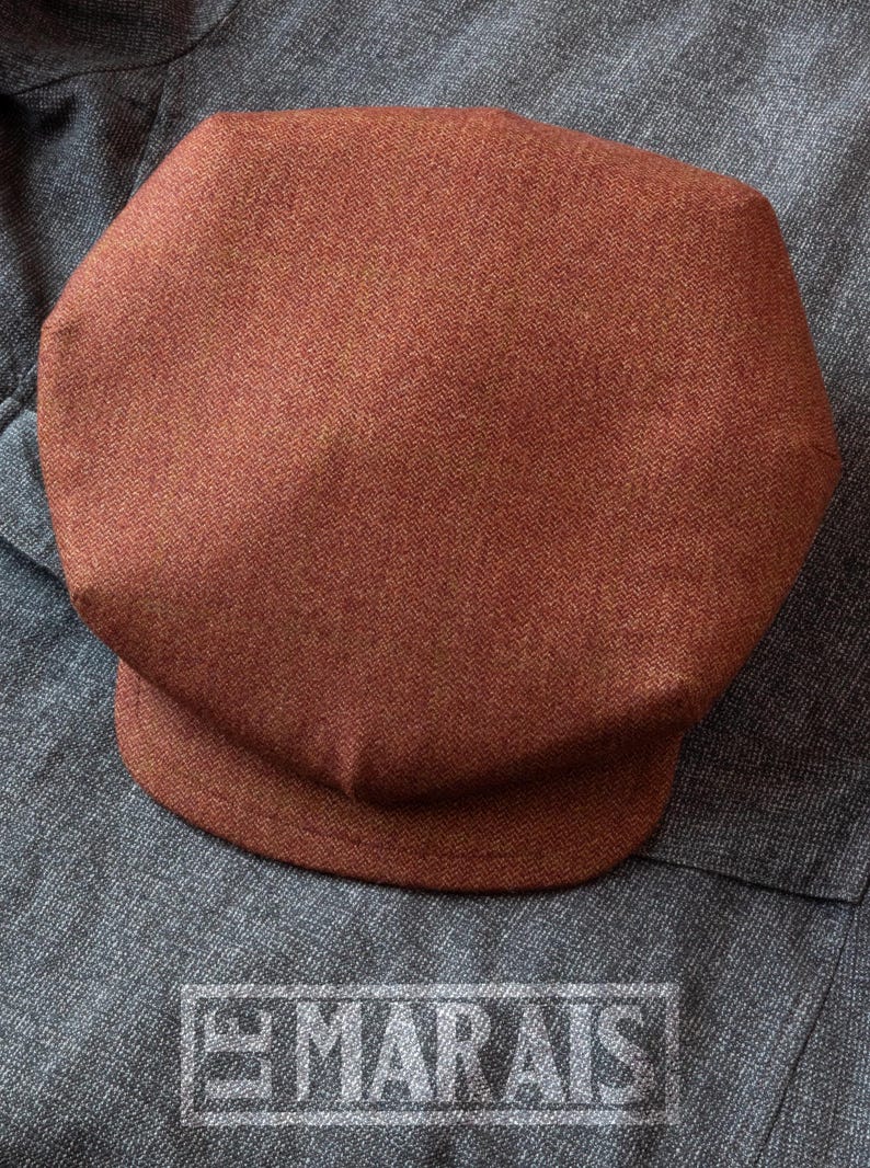 Puede incluir: Una gorra de newsboy de tweed marr&oacute;n con un patr&oacute;n de espiga.