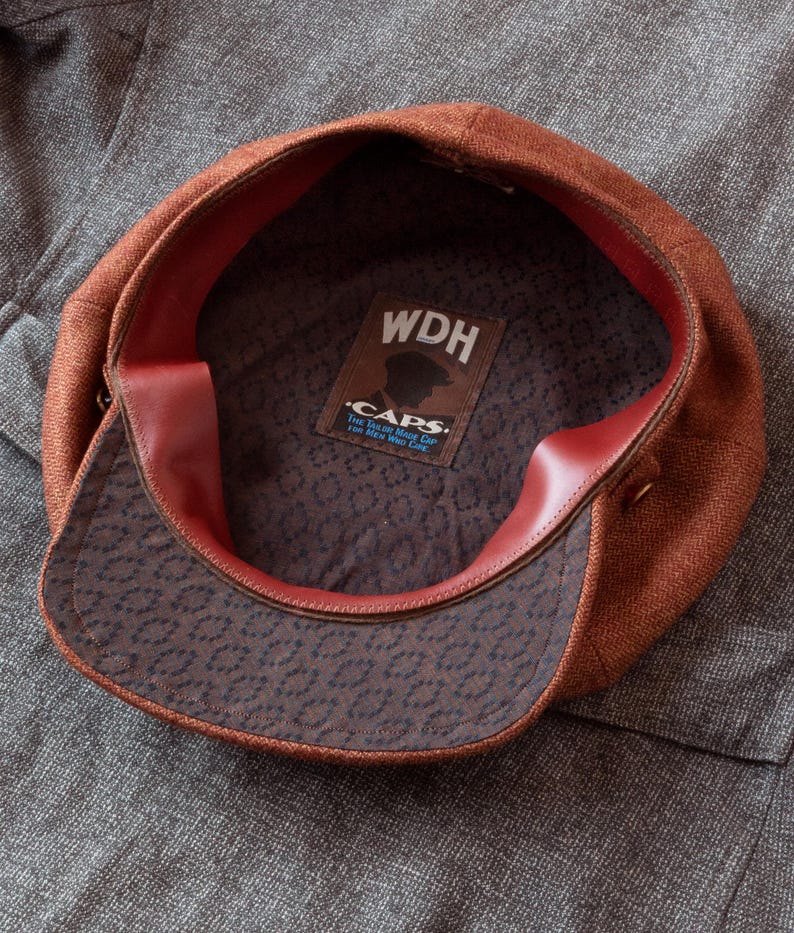 Puede incluir: Una gorra de newsboy de tweed marr&oacute;n con forro de cuero rojo. El interior de la gorra tiene una etiqueta que dice "WDH Caps. The True Made in Maine Cap.  For All Who Wear Caps."