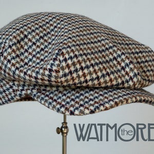 May include: A brown, black, and white patterned tweed newsboy cap. The cap is on a display stand. The text "WATMORE the" is visible in the lower right corner of the image.