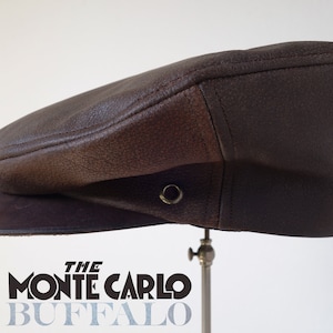 Puede incluir: Una gorra de newsboy de cuero marrón con una visera de cuero marrón contrastante. La gorra tiene un pequeño ojal de metal en la parte superior.