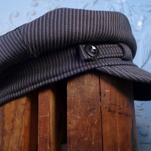 May include: A gray and black striped fabric newsboy cap with a button on the side.