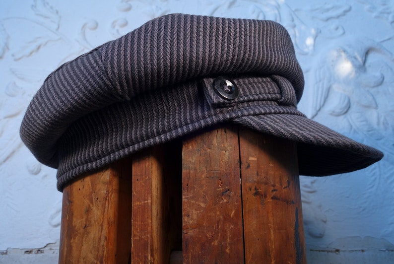 May include: A gray and black striped fabric newsboy cap with a button on the side.