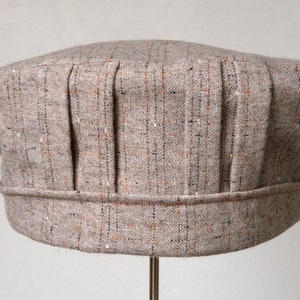 Puede incluir: Un gorro de chef de tela texturizada beige y marrón con pliegues.