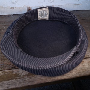 May include: A black and gray striped fabric hat with a circular label that says "HOM" in white lettering.
