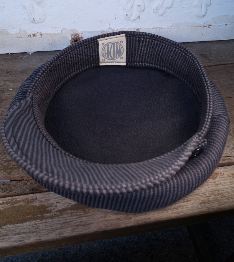 May include: A black and gray striped fabric hat with a circular label that says "HOM" in white lettering.