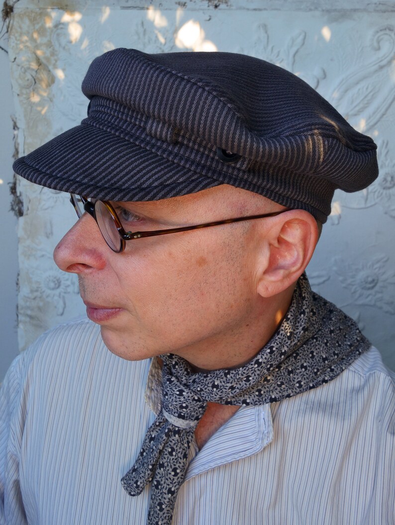 May include: A person wearing a striped, dark gray, flat cap with a black and white patterned scarf. The person is wearing a light blue, striped shirt.