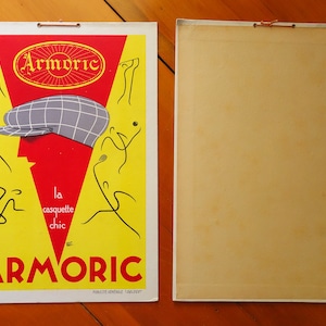 May include: A vintage advertisement for Armoric brand caps. The ad features a red and yellow background with a stylized illustration of a person wearing a plaid cap. The text reads "Armoric, la casquette chic".