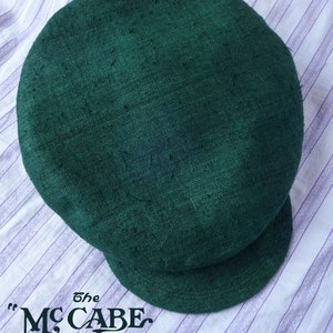 May include: A dark green, flat-brimmed straw hat with the text "the Mc CABE SUMMER STRAW" printed on the bottom.