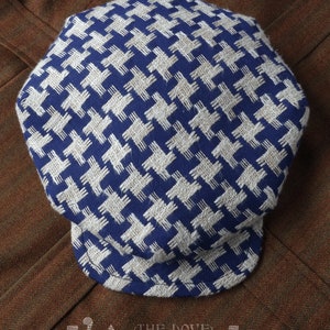 May include: A blue and white patterned newsboy cap with a brim. The cap is made of a woven fabric and has a slightly rounded crown. The brand name "L'Aironde" is visible on the bottom of the image.