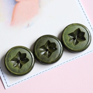 May include: Three green plastic buttons with a star-shaped design. The buttons have four points on the star and a hole in the centre.