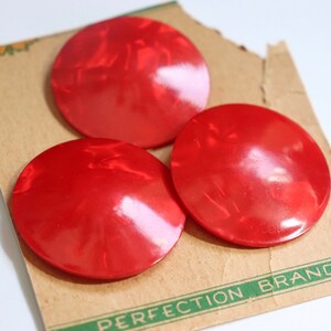 May include: Three large, round, red plastic buttons with a shiny finish. The buttons are on a brown card with green text that reads "Perfection Brand".