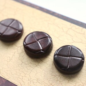 Peut inclure: Quatre boutons en cuir marron avec un motif en point de croix.