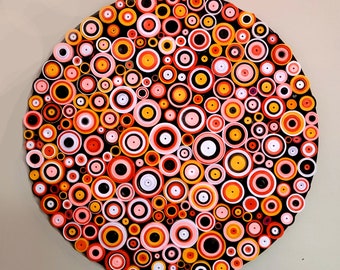 May include: A circular wall art piece made of paper, featuring a pattern of concentric circles in shades of orange, pink, white, and black.