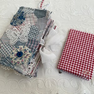 Pode incluir: Um diário artesanal com uma capa de patchwork em tons de azul, branco e cinza, adornado com uma borboleta de renda branca e detalhes florais. Um caderno menor xadrez vermelho e branco com as iniciais "F.R." também está presente.