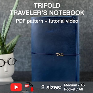 Può includere: Un taccuino da viaggio trifold blu scuro con un ciondolo infinito color oro. Il testo sull'immagine recita "TRIFOLD TRAVELER'S NOTEBOOK PDF pattern + tutorial video" e "2 sizes: Medium / A5 Pocket / A6".