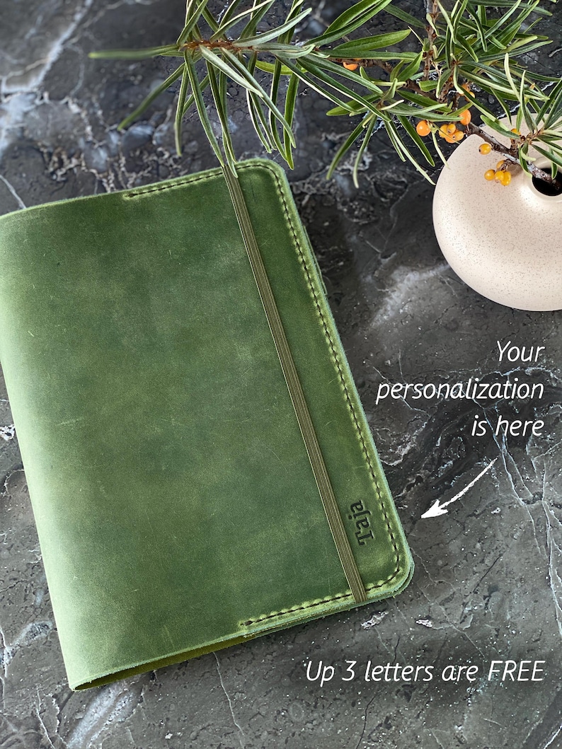 May include: A green leather journal with a stitched edge and a black elastic closure. The journal has the word "raja" embossed on the front cover. The text "Your personalization is here" is written on the image with an arrow pointing to the front cover. The text "Up 3 letters are FREE" is written below the journal.