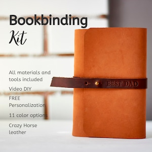 May include: A brown leather bookbinding kit with a strap and a brass buckle. The strap has the text "BEST DAD" embossed on it. The kit includes all materials and tools needed to bind a book, and comes with a video tutorial.