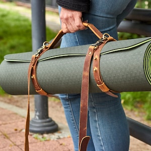 May include: A rolled-up green yoga mat with a brown leather carrying strap. The strap has a buckle and is adjustable.