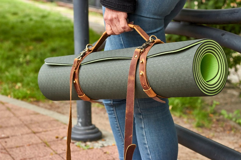 May include: A rolled-up green yoga mat with a brown leather carrying strap. The strap has a buckle and is adjustable.