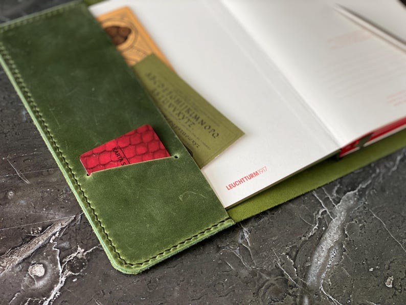 May include: A green leather notebook cover with a red card holder and the text "LEUCHTTURM1917" on the inside of the cover.