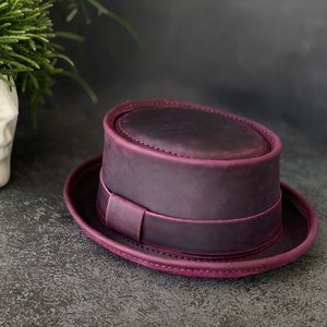 May include: A purple leather fedora hat with a wide brim and a band around the crown.