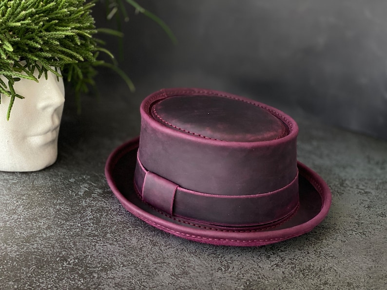 May include: A purple leather fedora hat with a wide brim and a band around the crown.